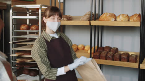 Frau-Mit-Maske-Und-Handschuhen,-Die-Brot-In-Der-Bäckerei-Verkauft