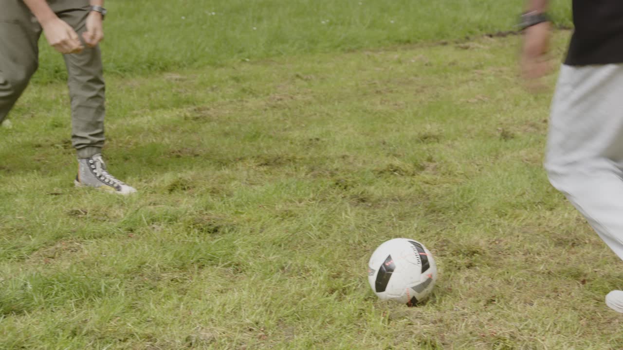 un joven negro y un hombre blanco jugando al fútbol en un parque y riendo