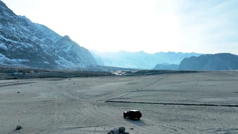 Off-road-vehicle-driving-across-the-vast-Sarfaranga-Cold-Desert-with-towering-snow-capped-mountains