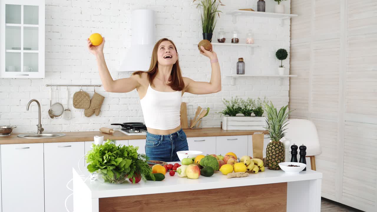 Funny and joyful girl dancing in the kitchen with fresh fruits in her hands. Good morning mood, healthy diet