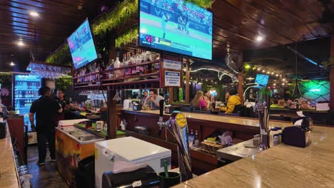 Interior view of a lively bar or restaurant with patrons, drinks, and sports playing on multiple televisions