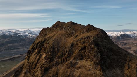 drone shot of a rugged rocky peak in búrfell, iceland, with distant snow-capped mountains and valleys creating a dramatic, natural landscape