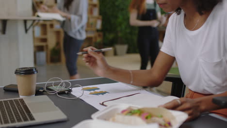 young african american business woman using laptop researching online using graph data writing notes working on project brainstorming in diverse office workplace close up