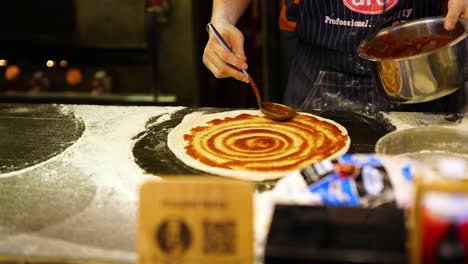 chef spreads sauce on pizza dough in krabi