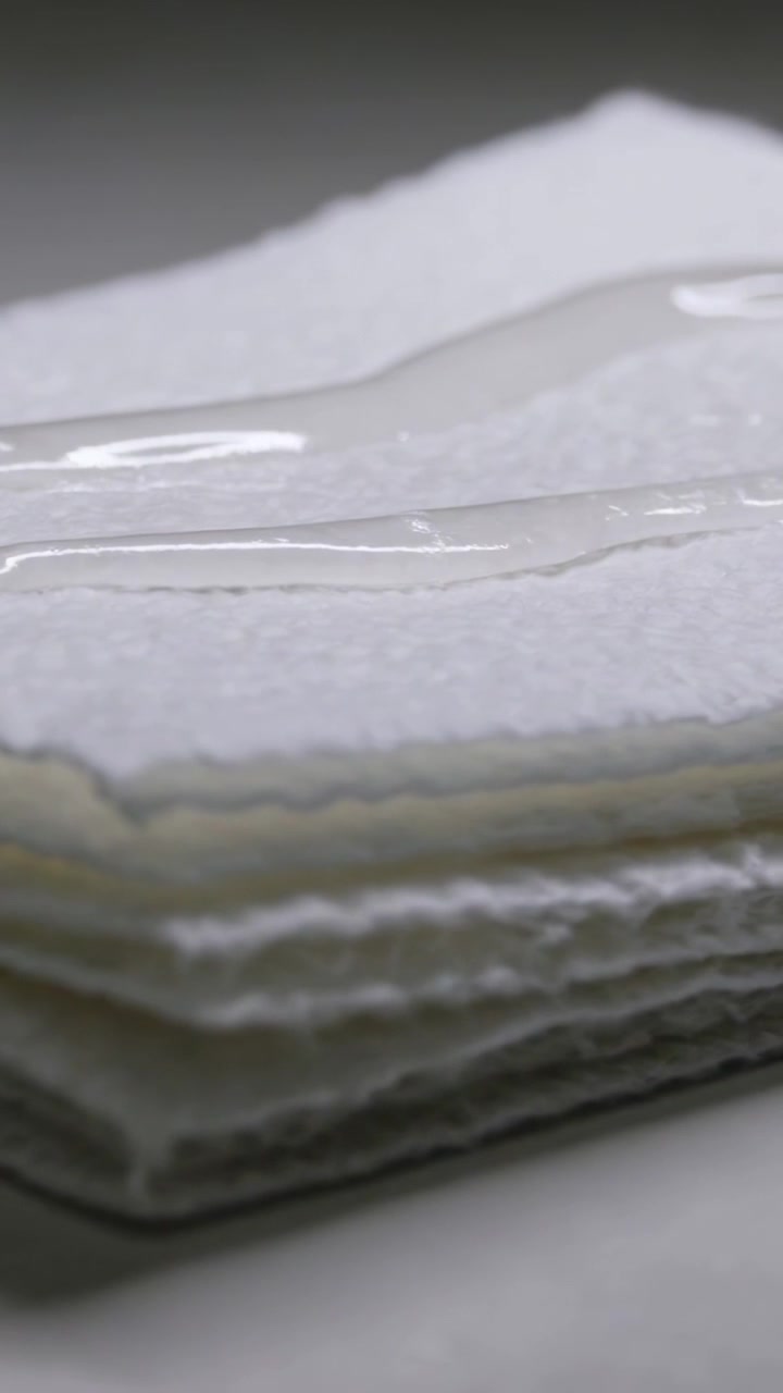 Vertical video: Showing sheet stack with clear gel bead appearing and spreading by tension on table