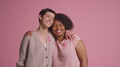 Retrato-De-Estudio-De-Dos-Mujeres-Orgullosas-De-Llevar-Cintas-Rosas-De-Concientización-Sobre-El-Cáncer-De-Mama-Abrazándose-Sobre-Un-Fondo-Rosa-2