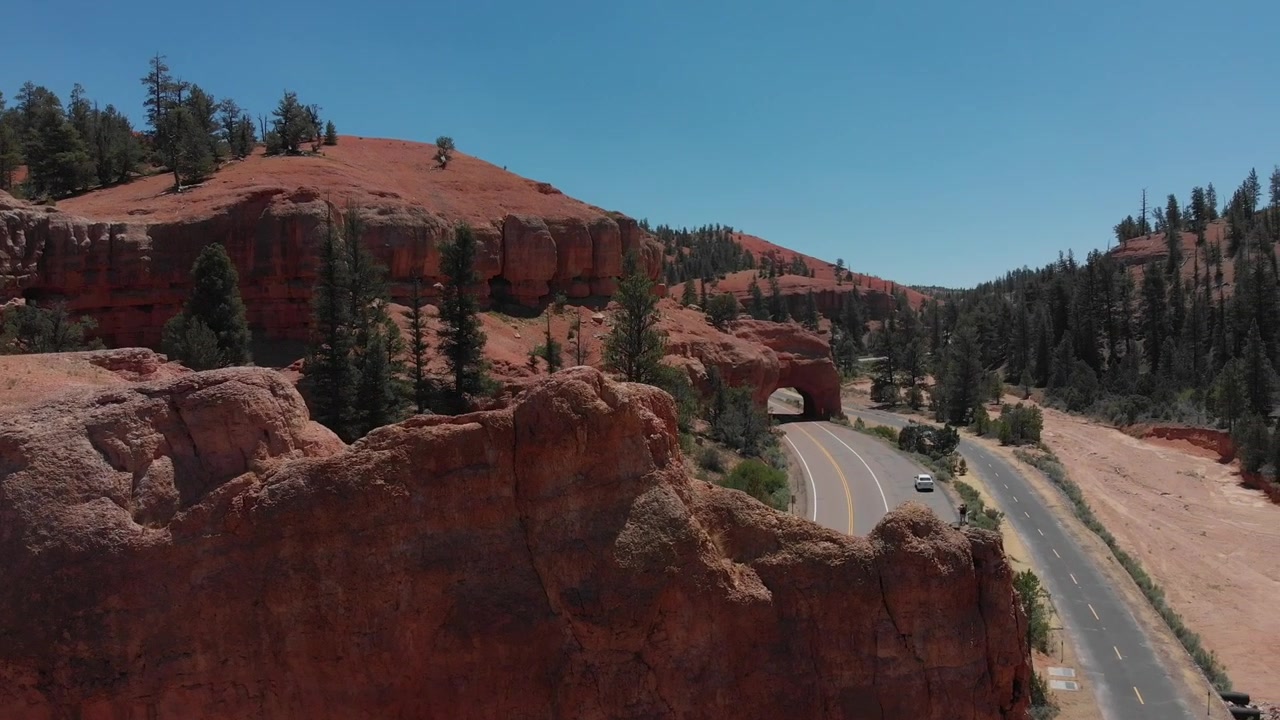 Un drone vola sopra un tunnel di roccia rossa e osserva l'area circostante con rocce rosse e pini.