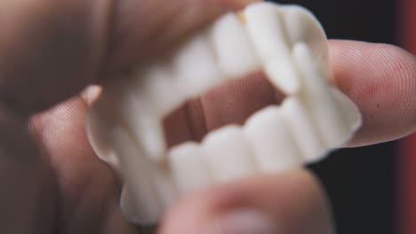 person plays with funny vampire teeth on black background