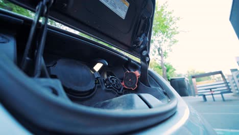 proceso de reabastecimiento de combustible de un automóvil eléctrico. un disparo debajo de la escotilla donde se carga el automóvil ecológico eléctrico. la escotella de carga del automóvil eléctrico se abre automáticamente. una mano masculina inserta un automóvil erecto