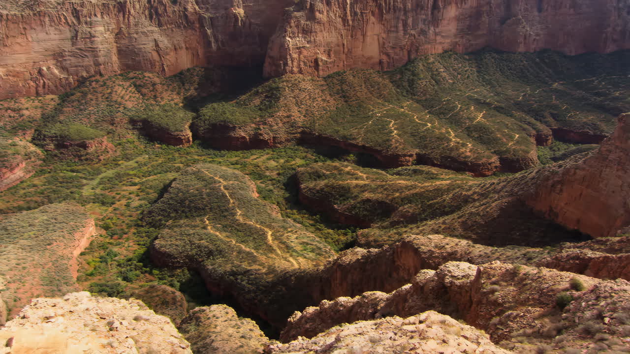 A vast canyon landscape with green vegetation and winding trails