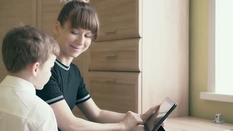 mother-shows-her-son-how-to-do-homework-smiling-uses-a-tablet-computer