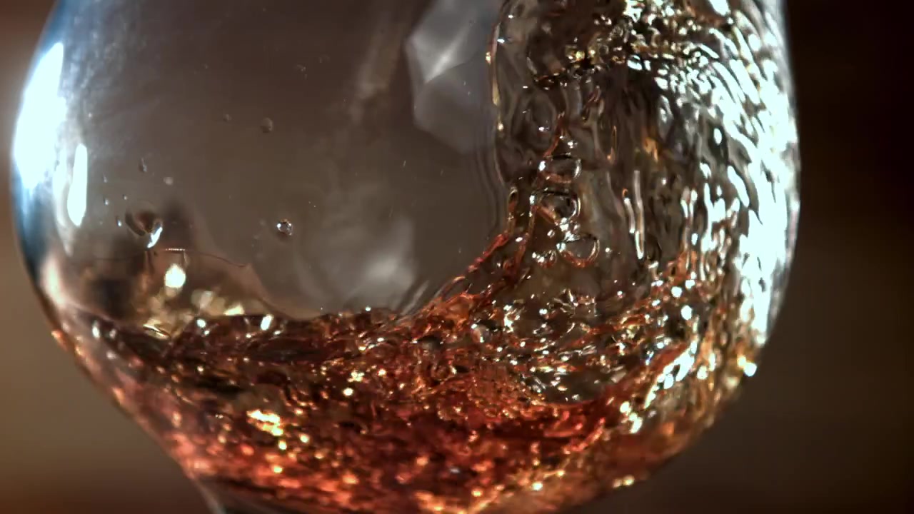 Liquido ambrato che vortica e riempie un bicchiere al rallentatore