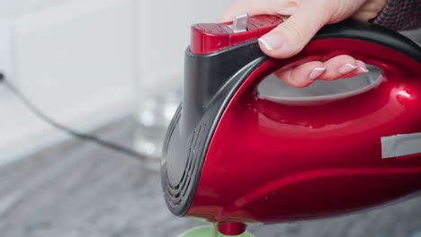 primer plano de una persona que sostiene un mezclador de mano eléctrico, mezclando ingredientes dentro de una taza verde, preparando bebidas, configuración de la cocina, encimera, fondo borroso