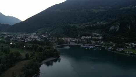 Eine-Faszinierende-Luftaufnahme-Von-Walensee-Und-Weesen-Zeigt-Das-Tiefblaue-Wasser,-Ein-Wohngebiet-Und-Die-Schweizer-Alpen-Im-Hintergrund