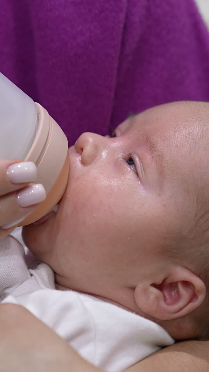 Mother is holding a child in her arms and feeding a baby from a bottle. Baby eating milk and falling asleep gradually. Close up. Vertical video