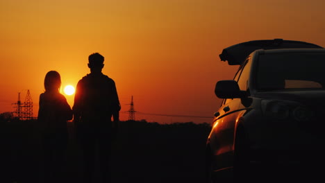 a young couple is standing near his car and admiring the sunset over the guesthouse