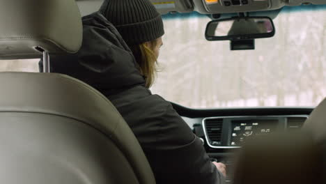 rear view of man turning on radio in his car on a winter day