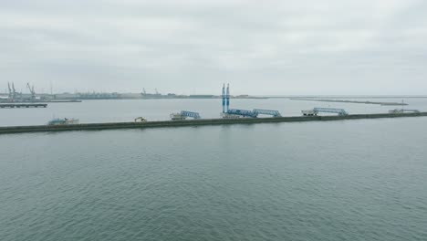 Aerial-establishing-view-of-port-cranes-and-empty-loading-docks-at-Port-Of-Liepaja-,-Liepaja-city-in-the-background,-overcast-summer-day,-wide-drone-shot-moving-forward