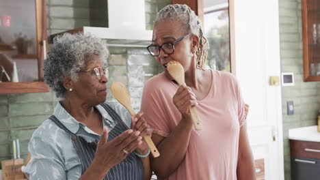 Happy-senior-african-american-female-friends-preparing-meal,-singing-in-kitchen,-slow-motion