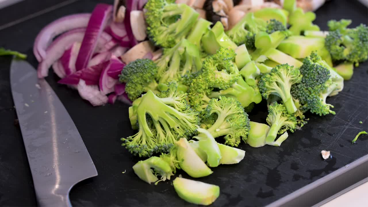 A chef's knife rests beside a pile of vibrant, freshly cut broccoli florets, mushrooms, and red onions. This culinary close-up captures the fresh ingredients for a healthy, gourmet meal