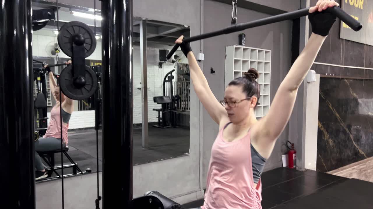 mujer con gafas haciendo ejercicio con una máquina de chin-up en el gimnasio, movimientos de ejercicio para los músculos del brazo