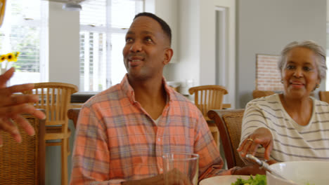 Front-view-of-young-black-woman-serving-food-to-her-family-at-dining-table-in-a-comfortable-home-4k