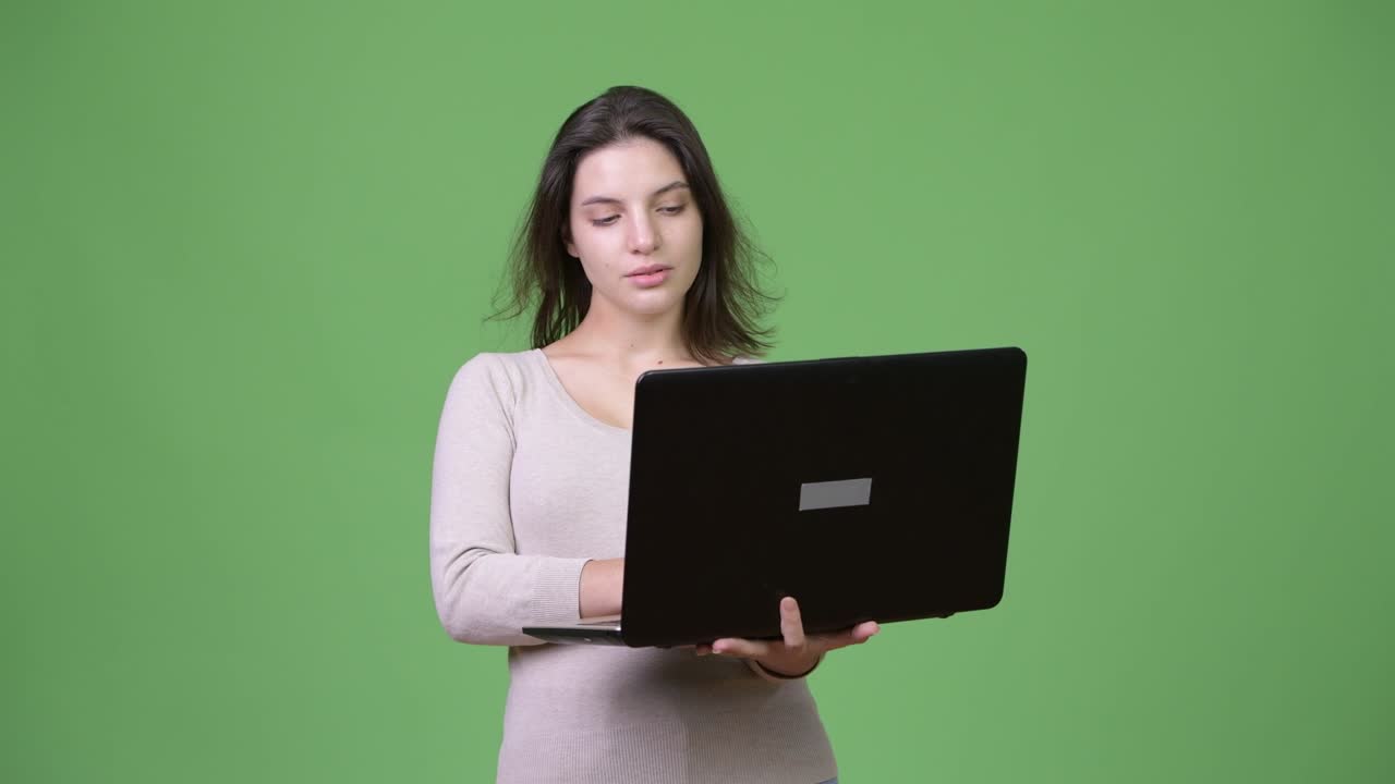 Young beautiful woman thinking while using laptop