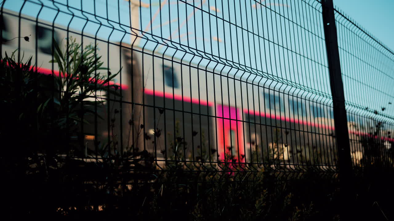 Blurred motion of a modern train seen through a wire fence with blue sky background