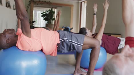 Diverse-seniors-using-exercise-balls-in-pilates-class-with-female-coach,-unaltered,-in-slow-motion