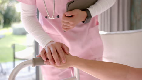 nurse in pink scrubs holding clipboard, assisting patient with walker