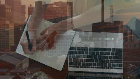 animación de las manos de una mujer de negocios caucásica usando una computadora portátil y tomando notas sobre el paisaje urbano