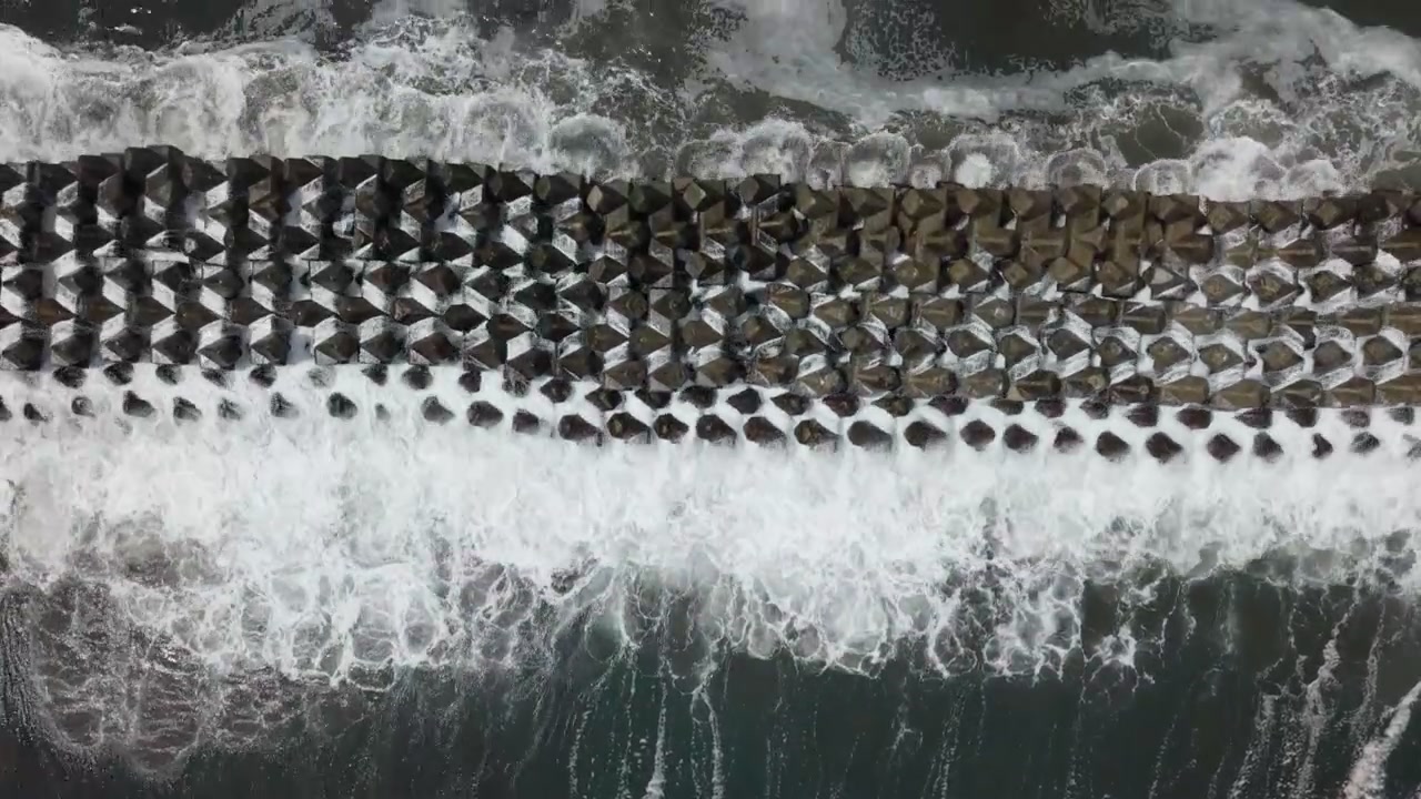 Onde scure dell'oceano che si infrangono e schiumano su una spiaggia sabbiosa sulla costa di Kawazu, Izu, Giappone, retroilluminate dalla luce bassa del sole, ripresa aerea con drone direttamente dall'alto