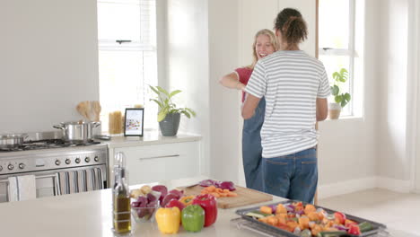 Happy-diverse-couple-wearing-apron-and-dancing-in-kitchen,-slow-motion