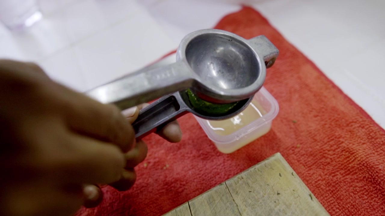 Vista ravvicinata di una mano che sprema un lime fresco in uno spremiagrumi di metallo sopra un piccolo contenitore, una semplice scena di cucina che mostra l'estrazione di agrumi per cucinare e preparare i pasti.