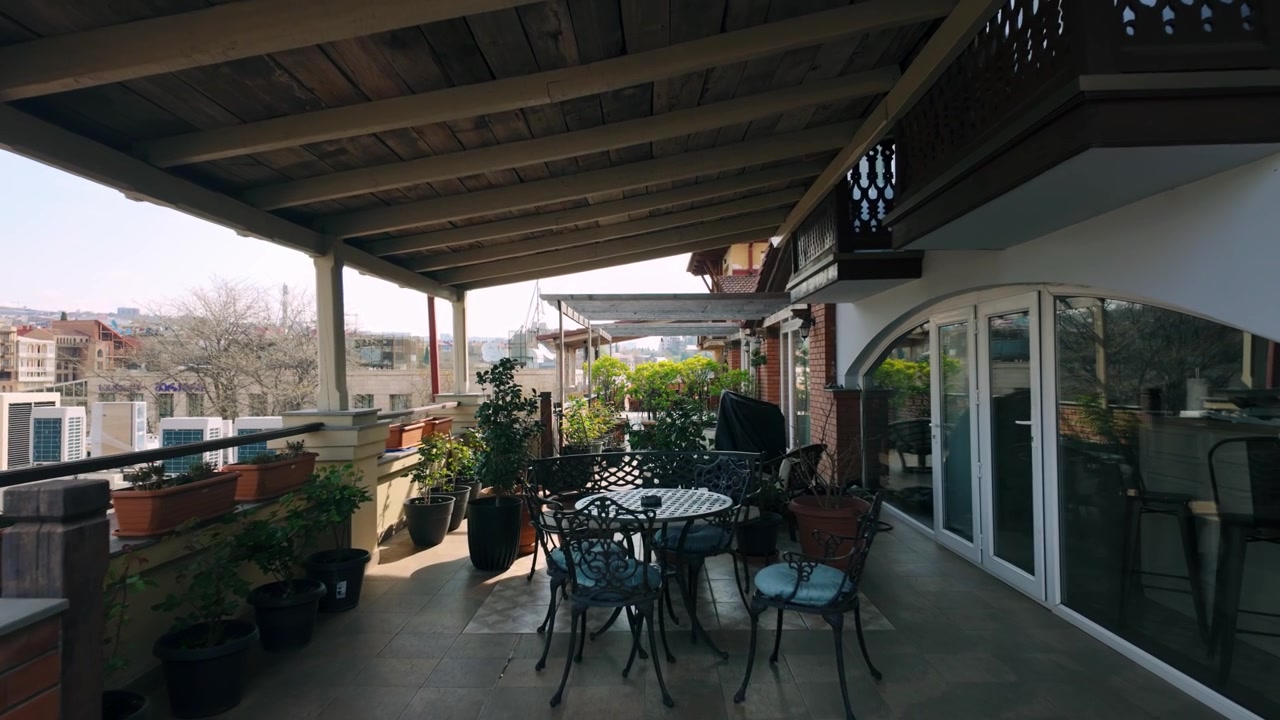 Accogliente patio esterno o balcone con mobili eleganti e piante in vaso, che offre una vista panoramica dello skyline di Tbilisi, Georgia, sullo sfondo. Perfetto per il relax e il piacere urbano