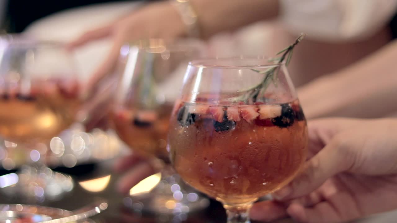 Inquadratura bokeh a mano libera di tre donne che sollevano i loro cocktail appena preparati.