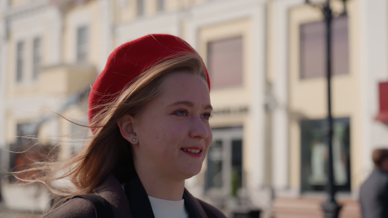 Donna che ride mentre cammina per una strada cittadina, berretto rosso e cappotto alla moda, la luce del sole le illumina i capelli, vetrine di boutique e pedoni sullo sfondo, atmosfera vivace di stile di vita urbano.