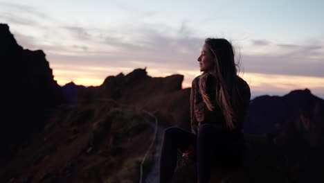 a woman sits peacefully on a mountain ledge, gazing at the sunrise over the peaks of madeira, portugal.