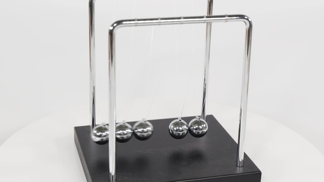 Chrome spheres on a Newton's cradle swing back and forth against a white studio background