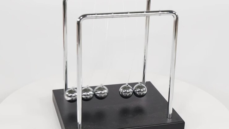 Chrome spheres on a Newton's cradle swing back and forth against a white studio background