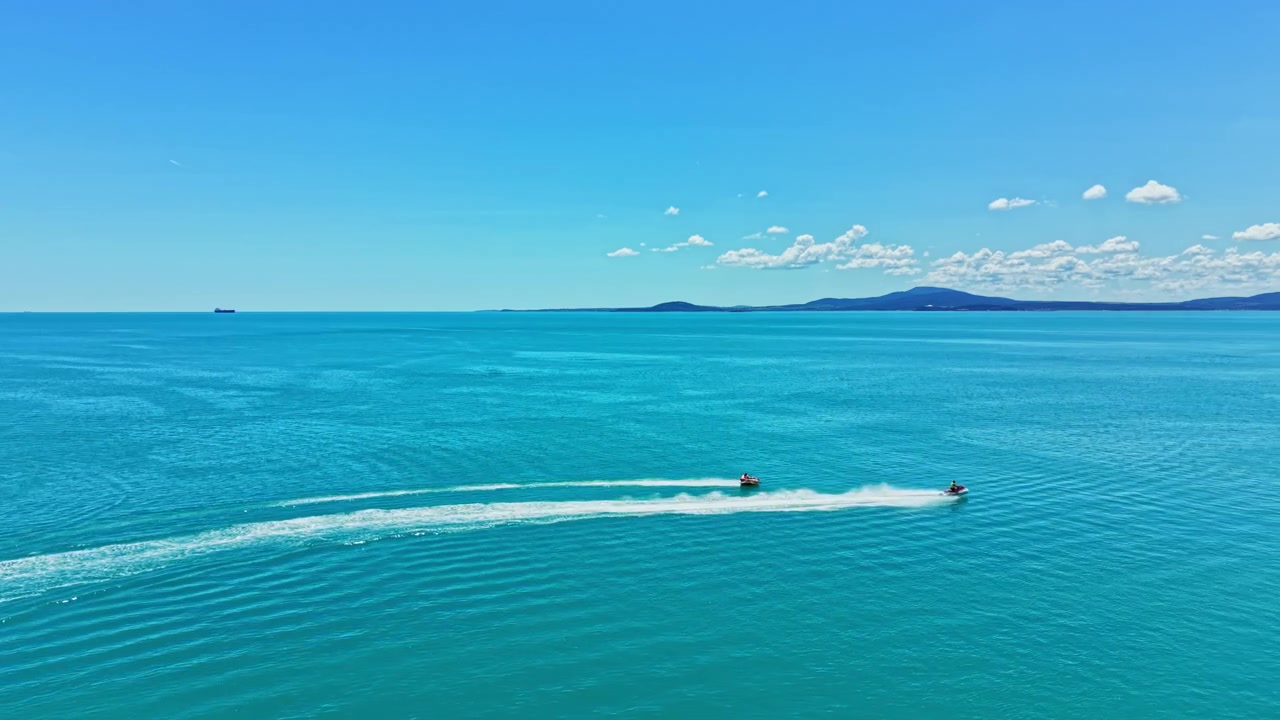 Due moto d'acqua scivolano su acqua limpida e blu vicino alla costa in una giornata di sole con qualche nuvola nel cielo