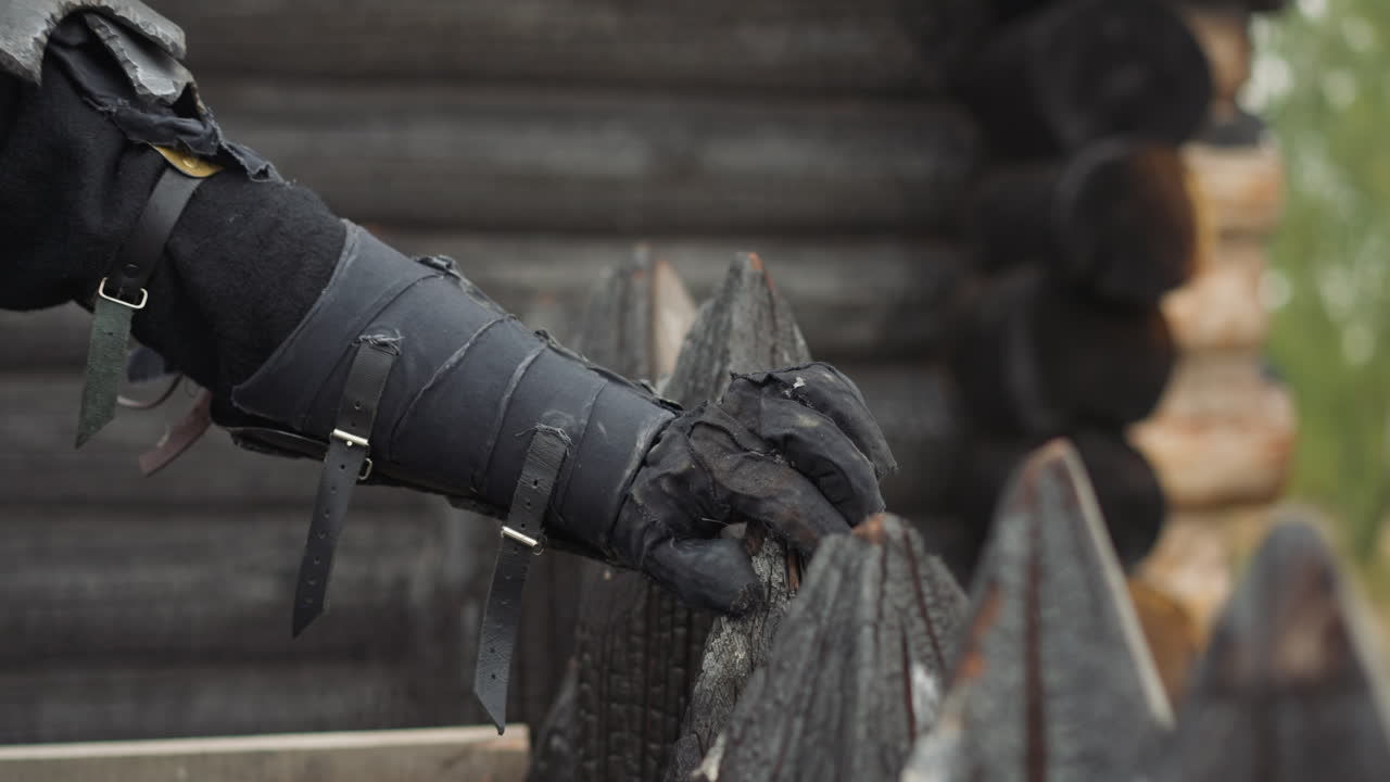 Black knight hand rests on spiky fence near burnt log house
