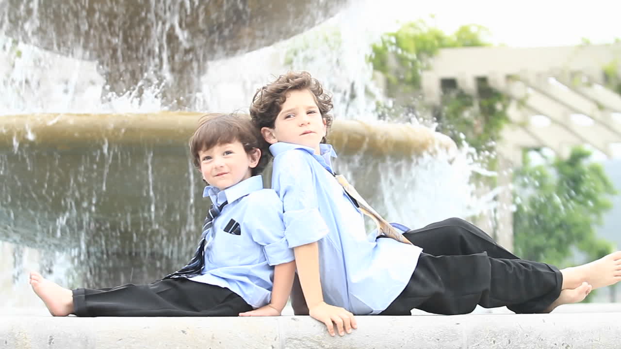 정장을 입은 한 쌍의 소년이 분수대 앞에 등을 맞대고 앉아 있다 1