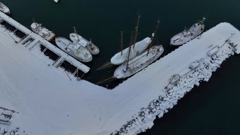 Backwards-drone-tilt-shot-of-historical-vessels-moored-in-Husavik-in-Iceland