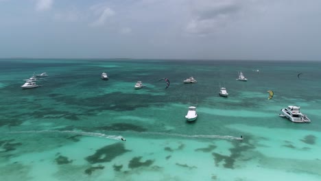 Kitesurfistas-Navegan-Persiguiéndose,-Yates-Anclados-Frente-A-La-Costa-De-Los-Roques,-Seguimiento-Aéreo