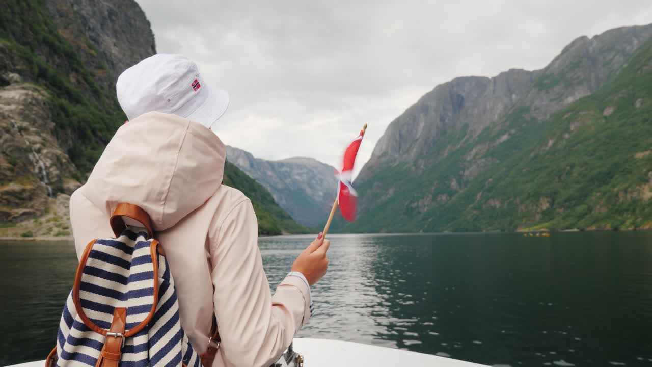 En turist med norsk flagg står på baugen av et cruiseskip Reise gjennom det pittoreske