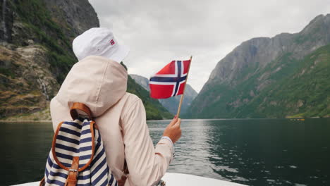 a tourist with a flag of norway stands on the nose of a cruise ship journey through the picturesque