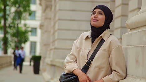 muslim businesswoman wearing hijab and modern business suit standing outside city office buildings