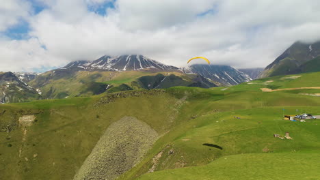 wide drone shot of a paraglider in gudauri georgia with the caucasus mountains in the distance