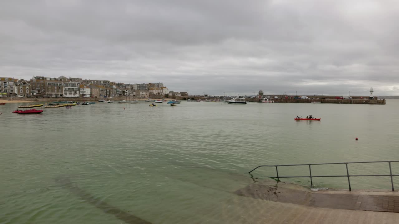 panning shot of St Ives harbour at high tide with a kayak paddling through